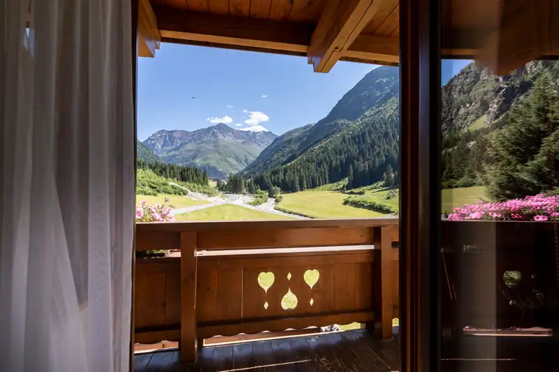 Blick vom Holzbalkon mit Herz-Ausschnitten auf das sommerliche Tal und die Berge