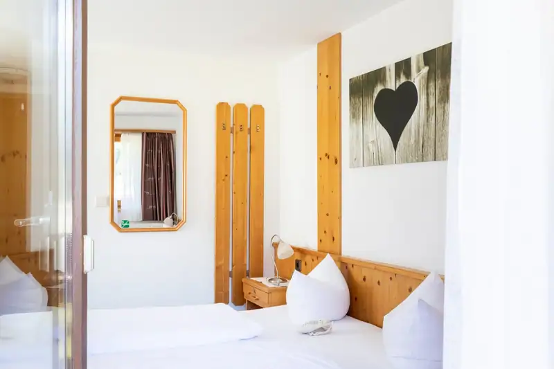 Zimmer mit Spiegel, Garderobe aus Holz und Bett mit weißen Kissen