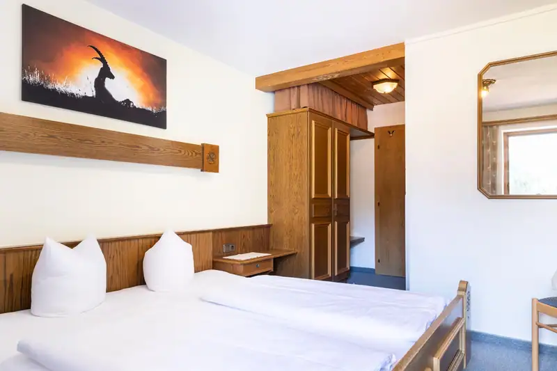 Doppelbett unter Steinbock-Bild, dahinter Kleiderschrank und Eingangsbereich